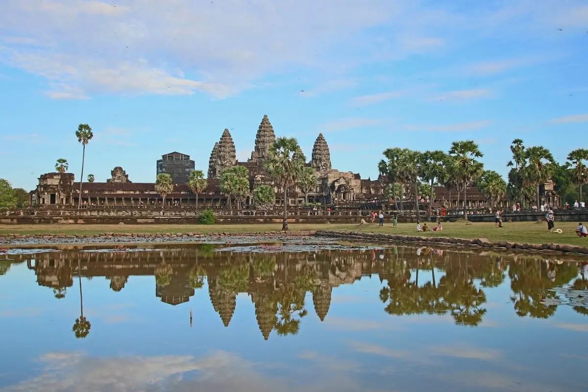 The spires of Angkor Wat reflected in a pool under a blue sky.