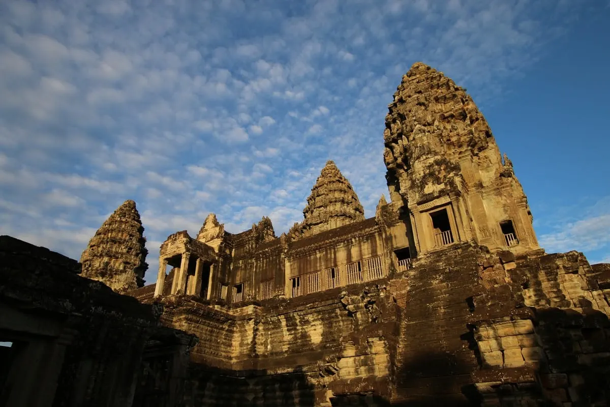 Sunlit stone towers of Angkor Wat against a blue sky with dappled clouds