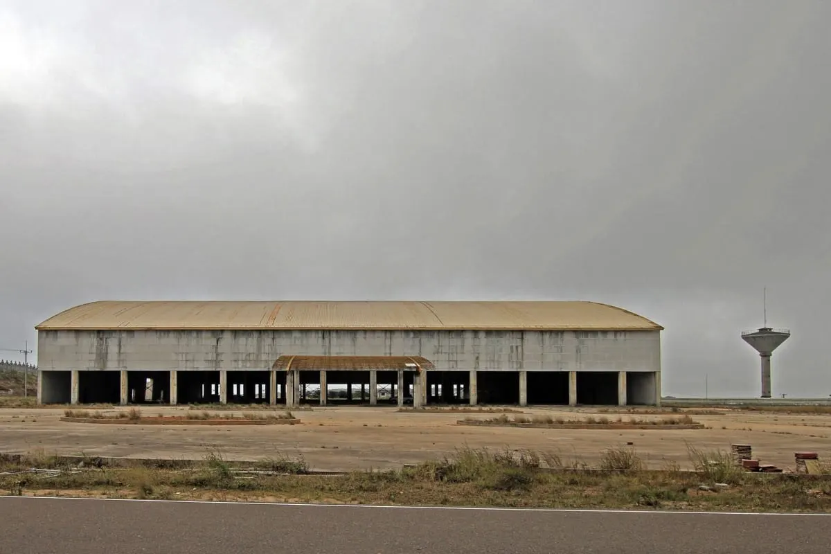 Empty hangar-like building and water tower under grey skies at Bokor Hill Station.