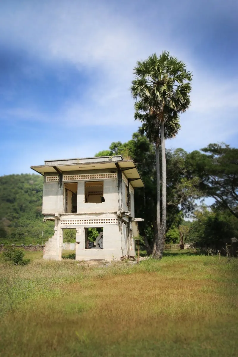 Abandoned two-storey villa shell beside a tall palm tree in Kep.