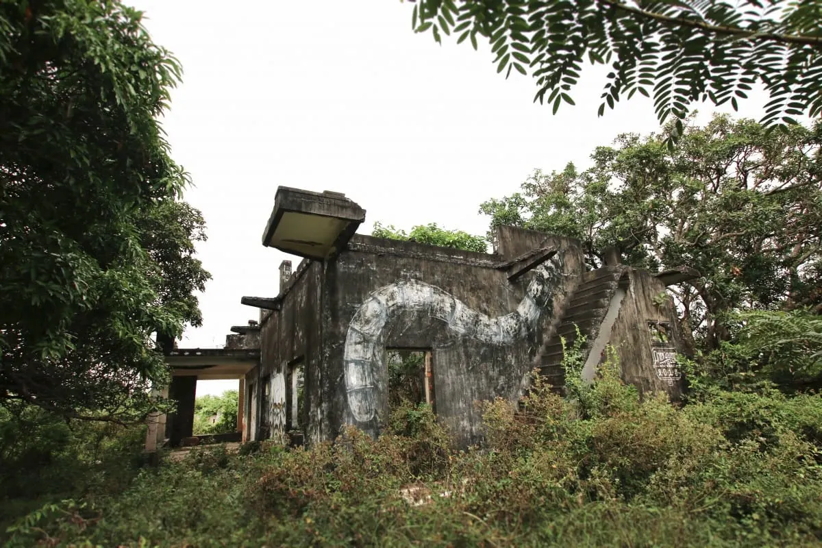 Overgrown ruin of a villa with a painted snake mural on its wall, Kep.