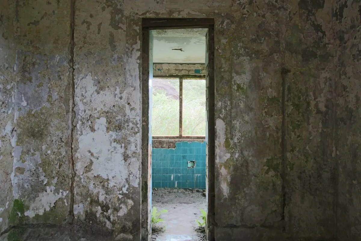 Doorway in a peeling wall opening onto a room with blue tiles, Kep ruin.