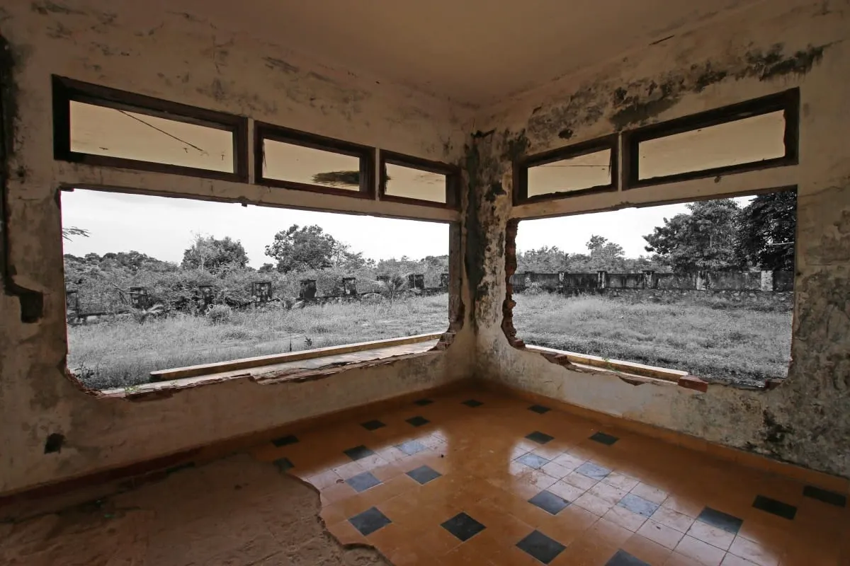 Empty room with tiled floor and window openings onto overgrown grounds, Kep.