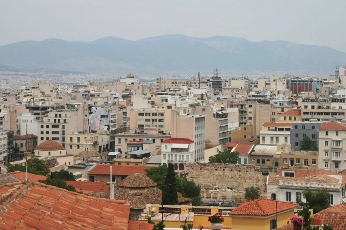 Terracotta rooftops and concrete apartment blocks of Athens beneath hazy mountains