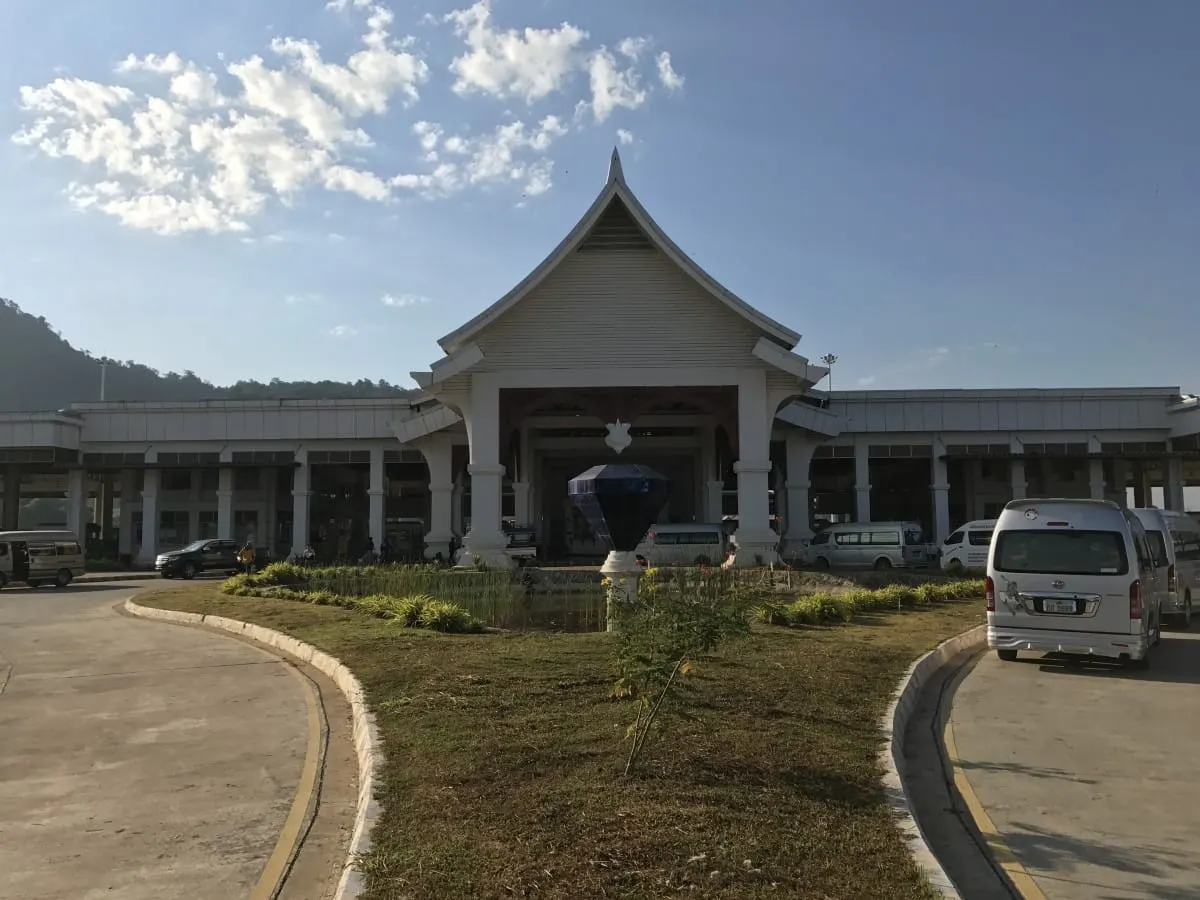 Border crossing building with peaked roof and minivans between Thailand and Laos