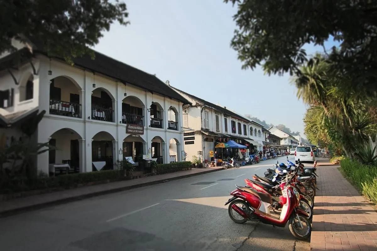 White colonial arcaded buildings and parked scooters on a quiet Luang Prabang street