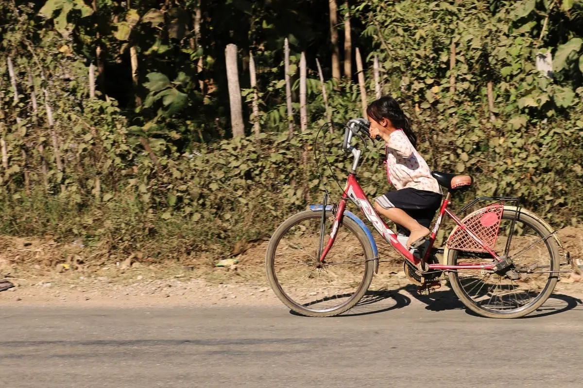 Young girl riding a red bicycle along a roadside in Laos
