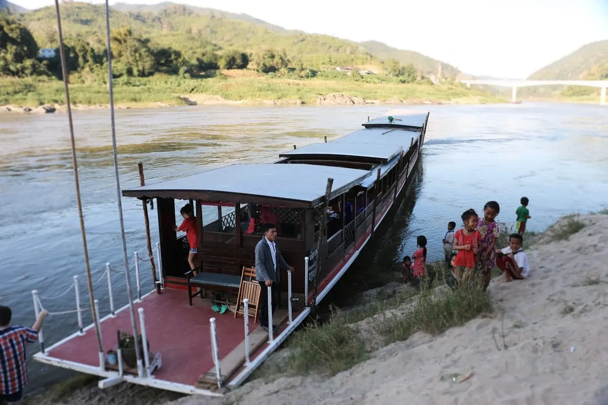 Slow boat moored at a sandy Mekong riverbank with village children nearby