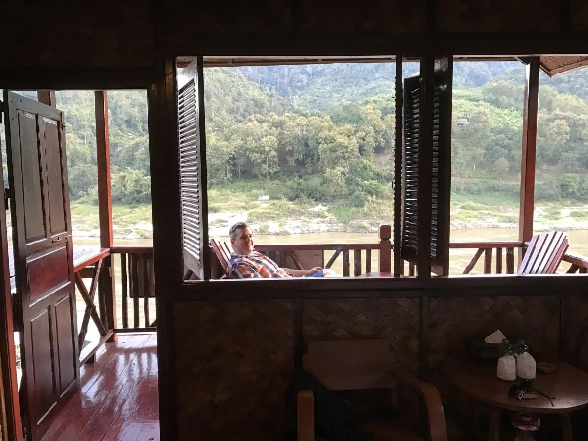 Man relaxing on a wooden balcony overlooking the Mekong at Pakbeng