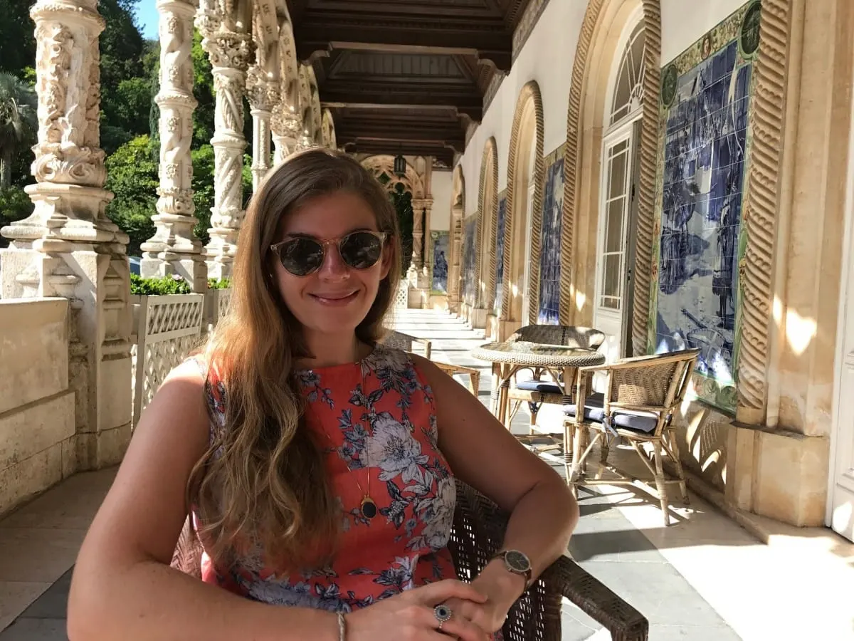 Smiling woman in sunglasses seated in the tiled stone arcade of Bussaco Palace