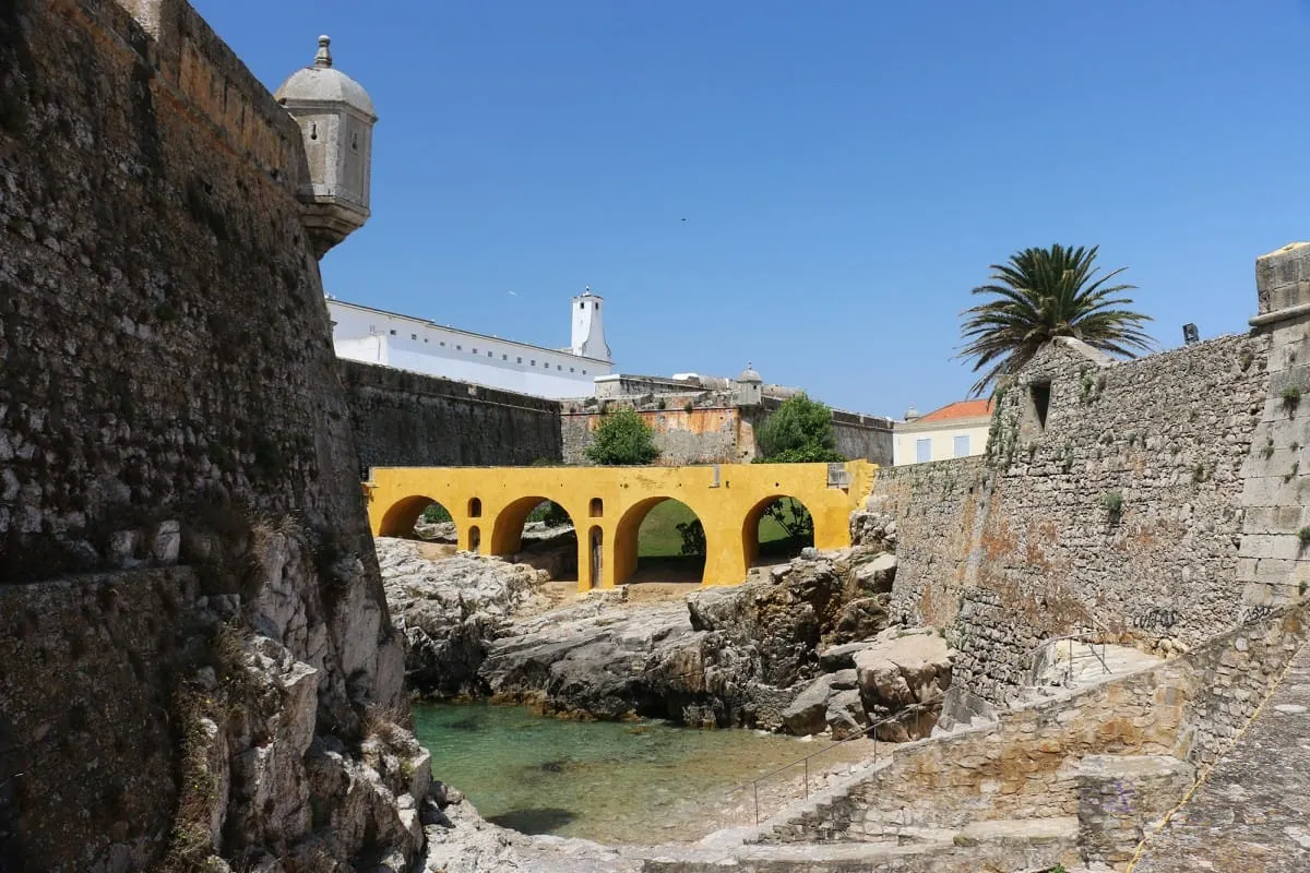 Stone walls of the Peniche fortress above a rocky inlet and yellow arched bridge