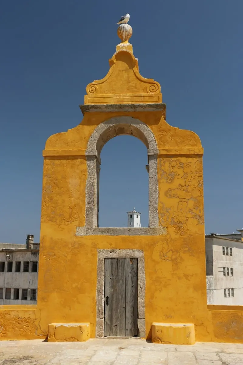 Yellow arched gateway with a seagull on top against deep blue sky