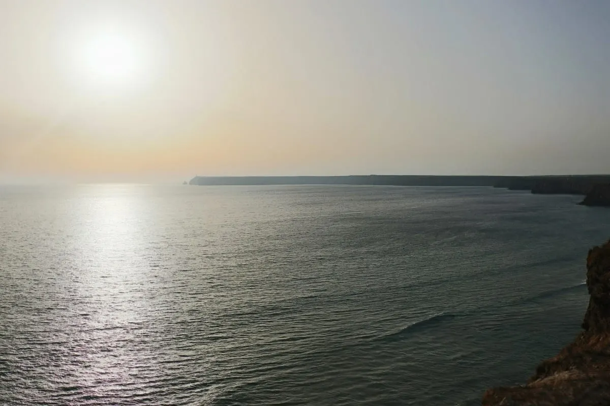 Hazy sun setting over the Atlantic and long cliff line near Sagres