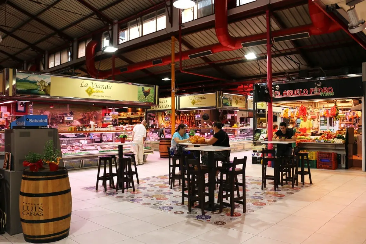 Butcher and fruit stalls with high tables inside a Madrid food market