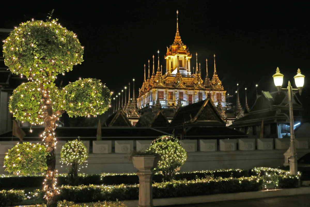 Loha Prasat spires glowing gold behind lit topiary at night