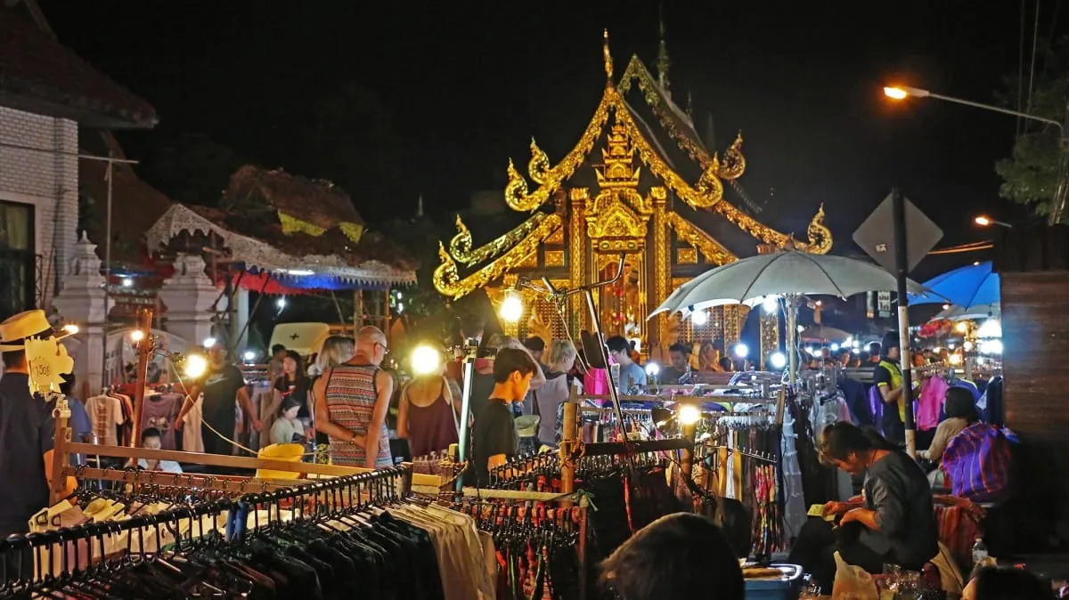 Clothing stalls and crowds at a night market before a gilded temple, Chiang Mai