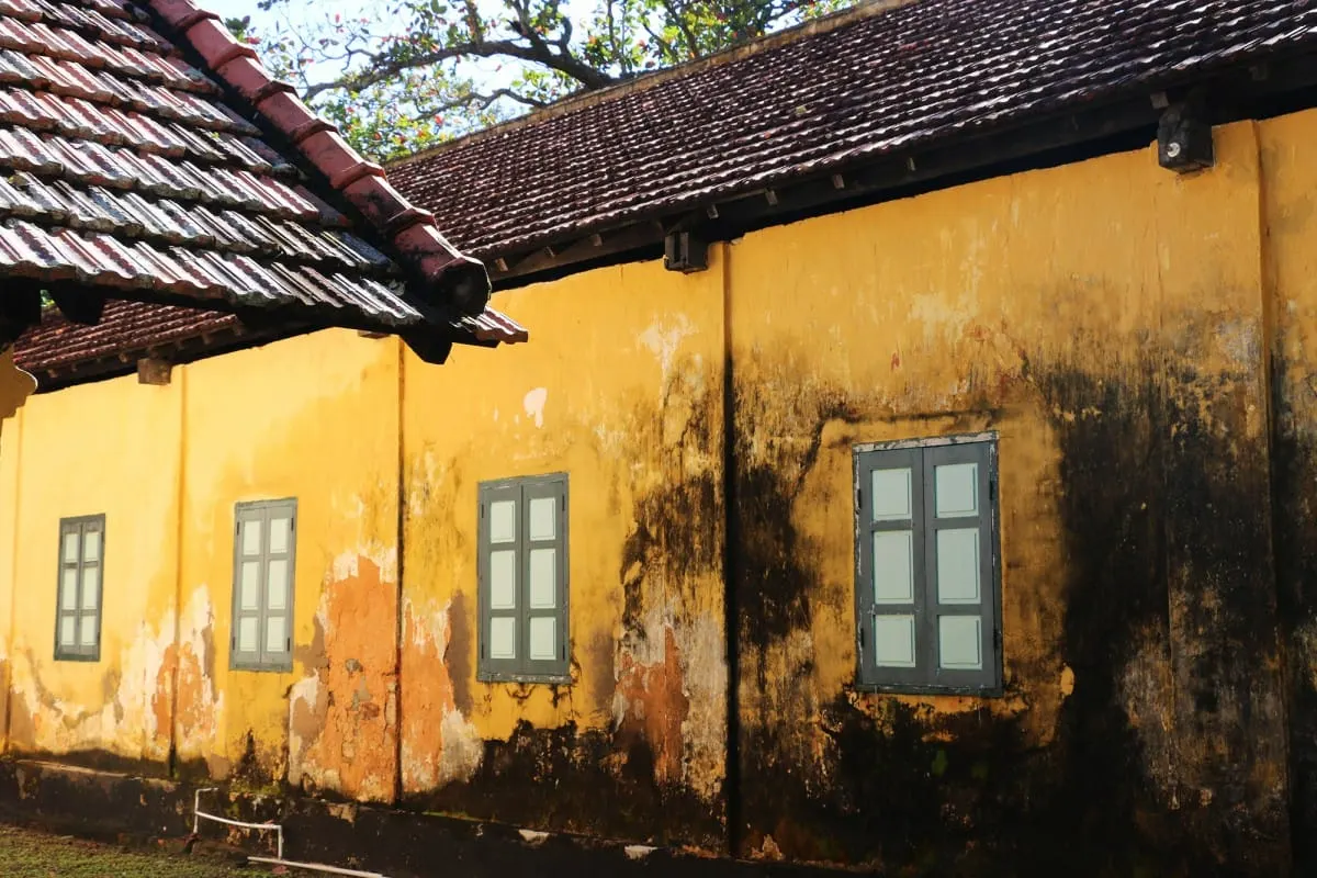 Weathered yellow prison wall with green shuttered windows under a tiled roof, Con Dao